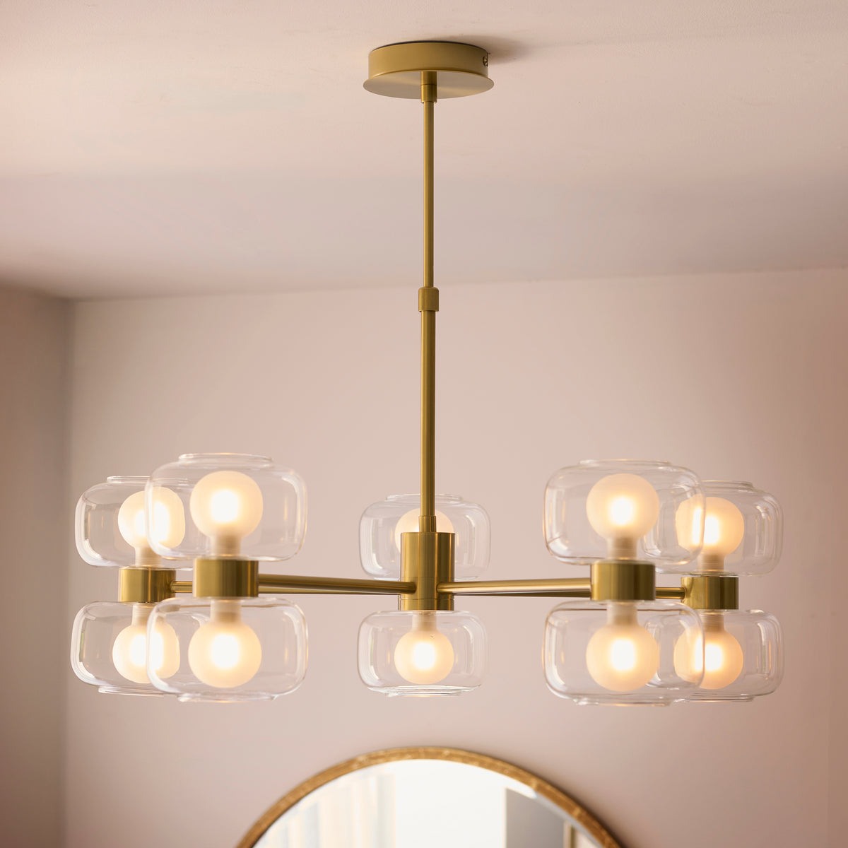 Rossano ten-light brass chandelier glowing beneath a white ceiling in a neutral room