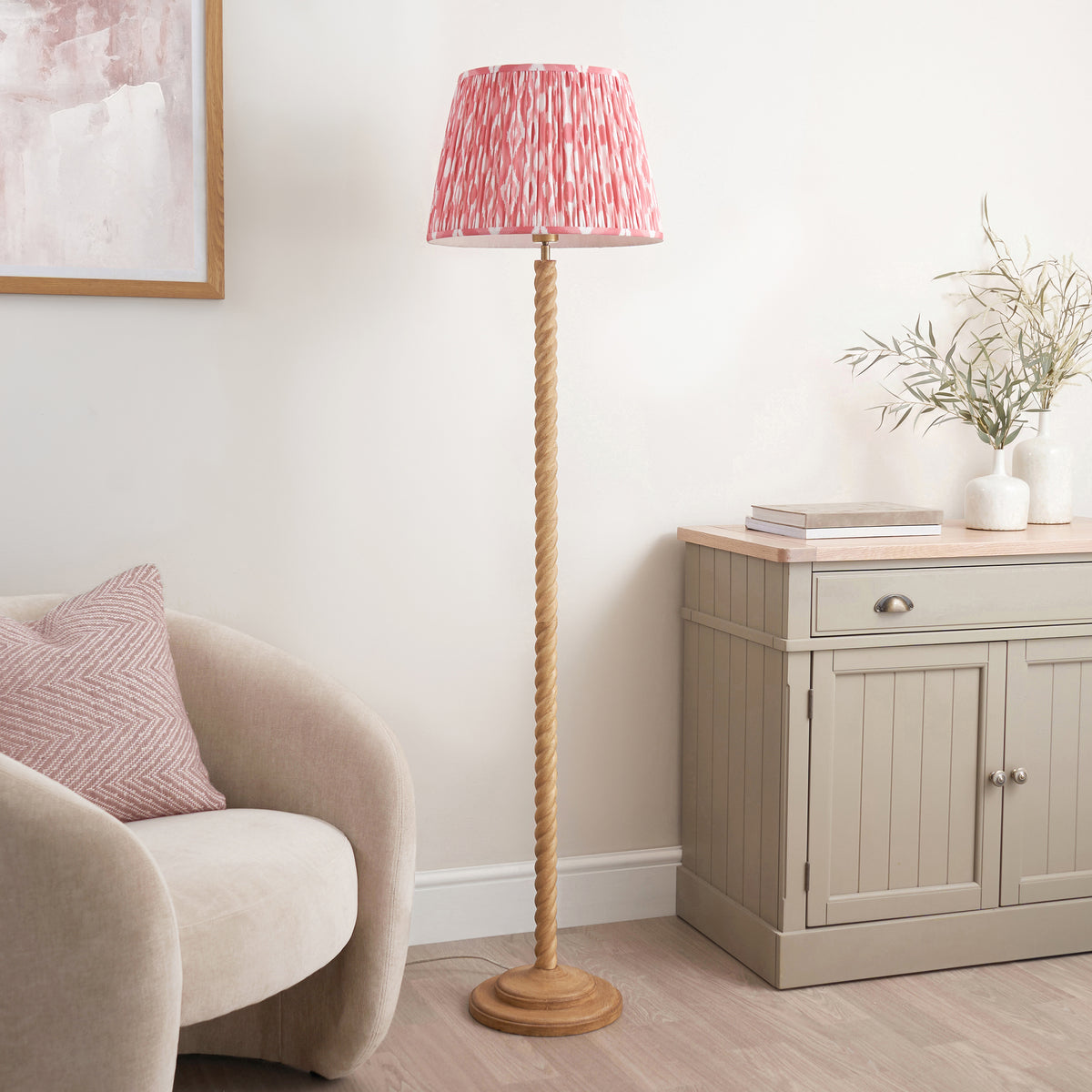 Oak effect twisted floor lamp with pink ikat shade beside a cream chair and sideboard
