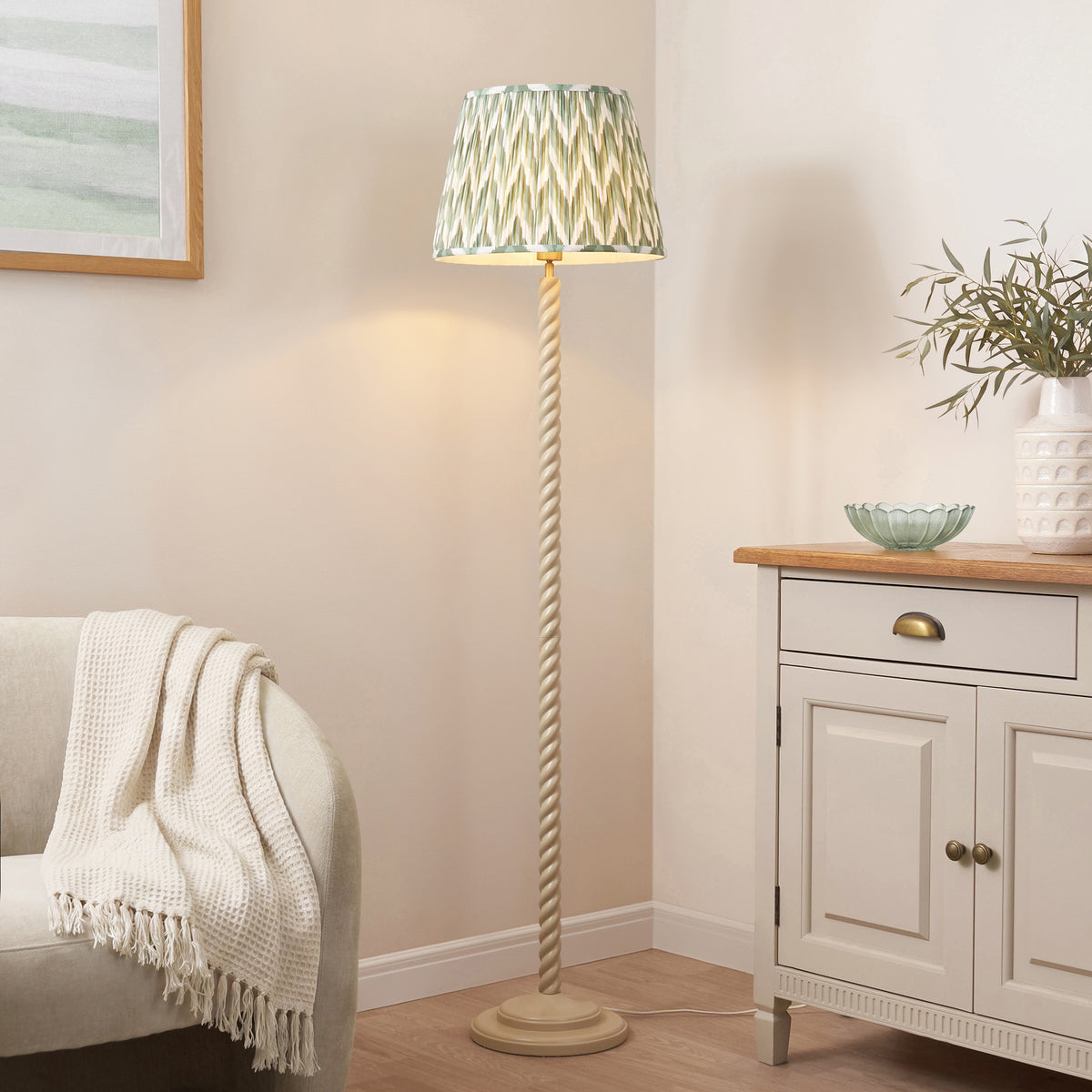 Cream twisted stem floor lamp with green zigzag shade beside an oak topped sideboard