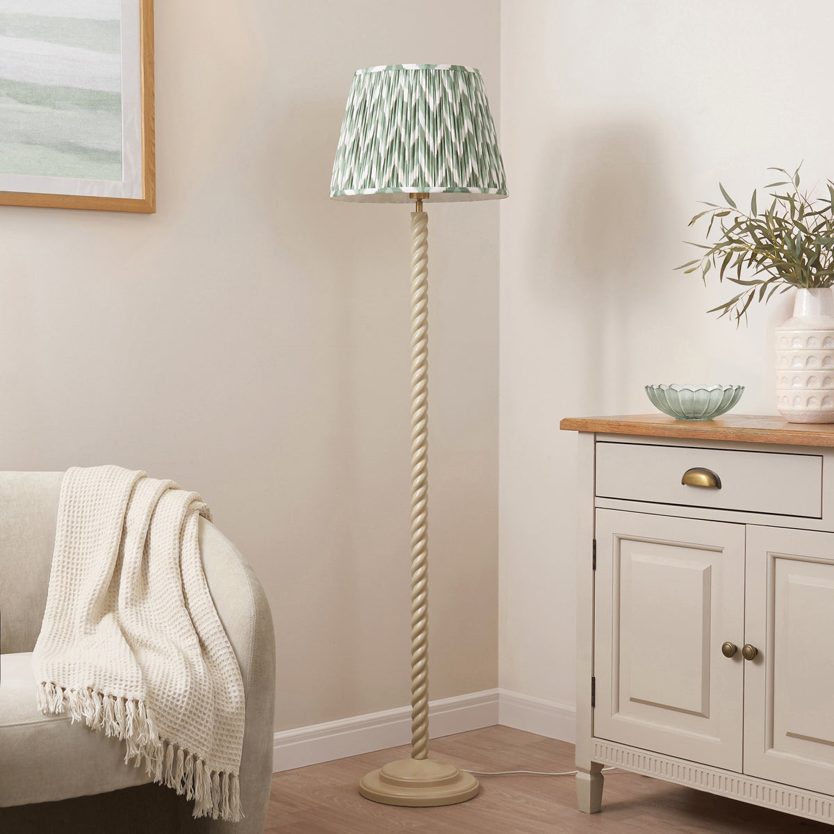 Green and white zigzag floor lamp in a living room corner with throw and potted olive