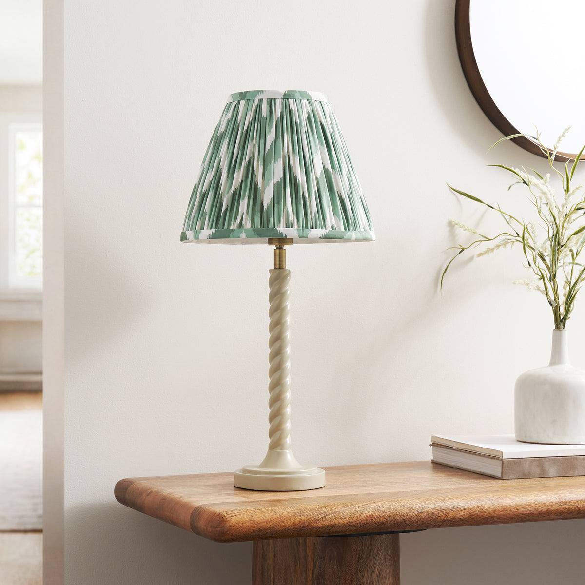 Almond white twisted table lamp with green zigzag shade on a wooden console beside a white vase