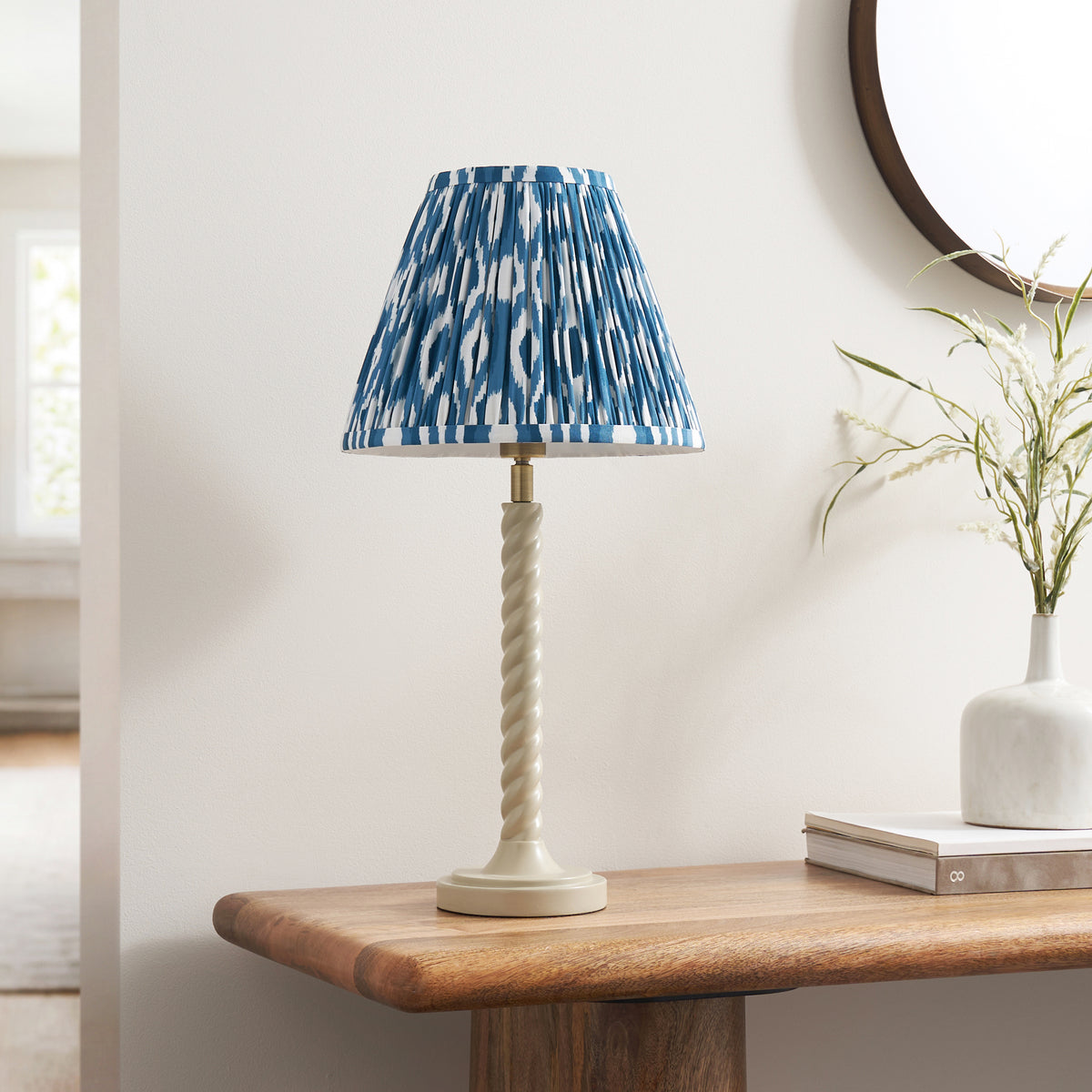 Almond white twisted table lamp with blue ikat pleated shade on a wooden console table