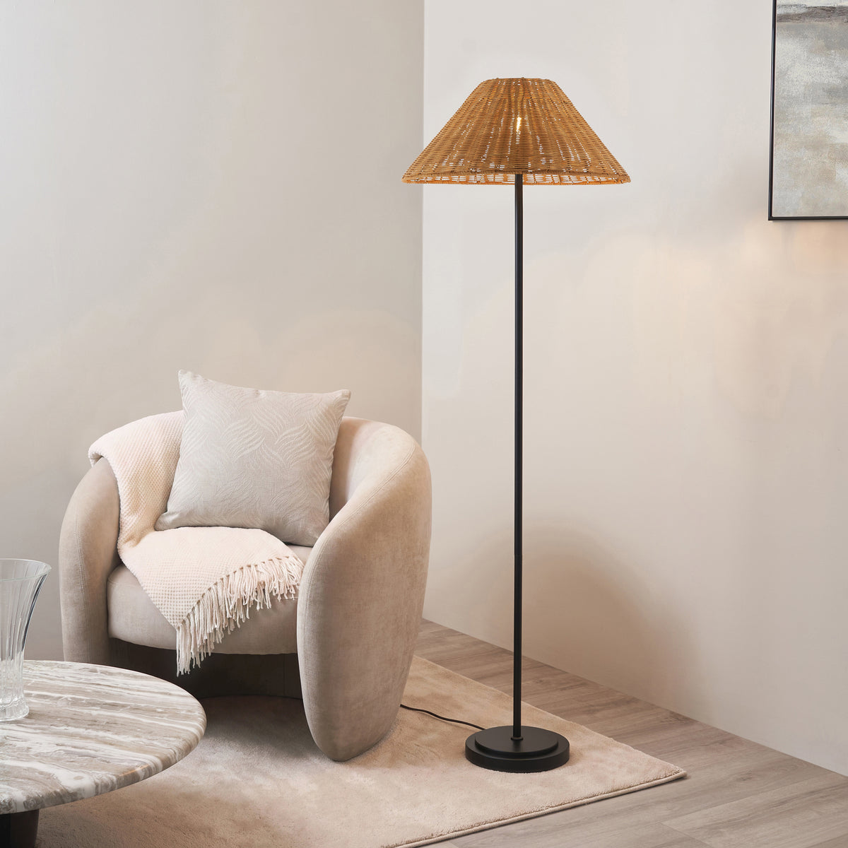 Arlo floor lamp with brown rattan shade lit beside a cream boucle armchair and round table