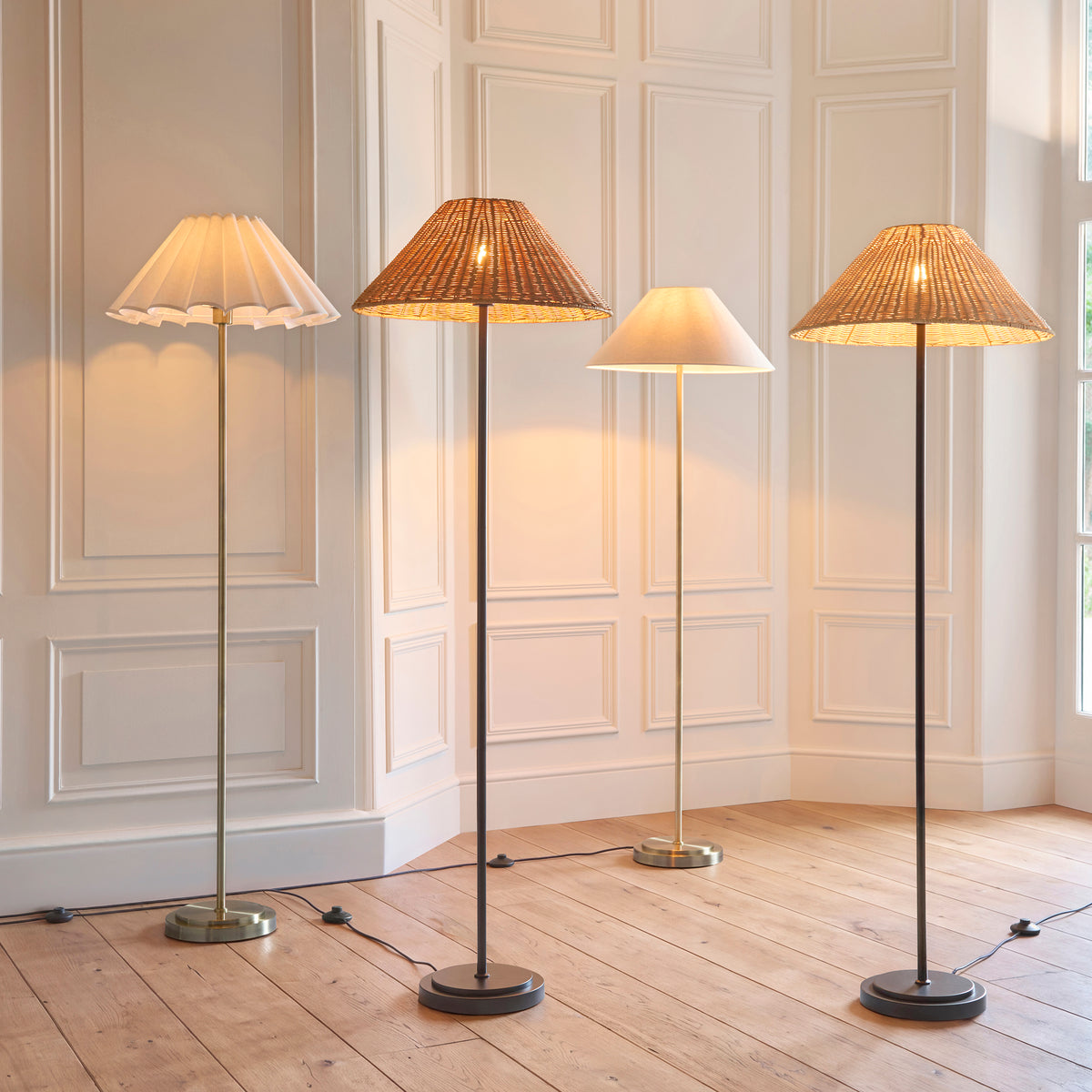 Four Arlo floor lamps with pleated, rattan and linen shades lit in a panelled room