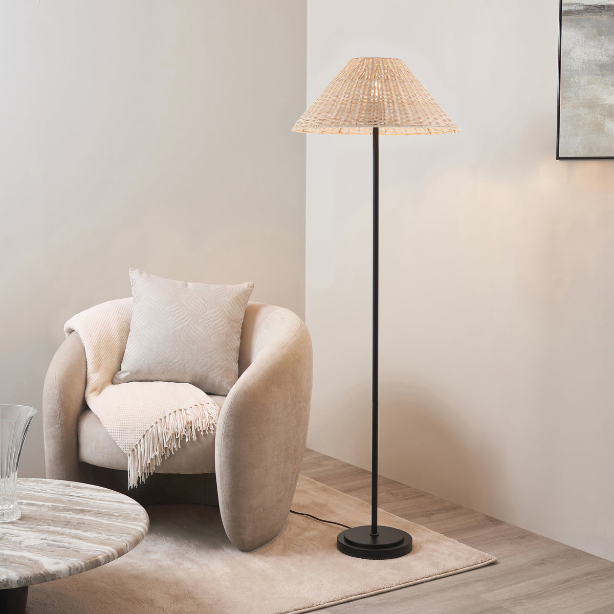 Arlo floor lamp with natural rattan shade lit beside a cream boucle armchair and cushion