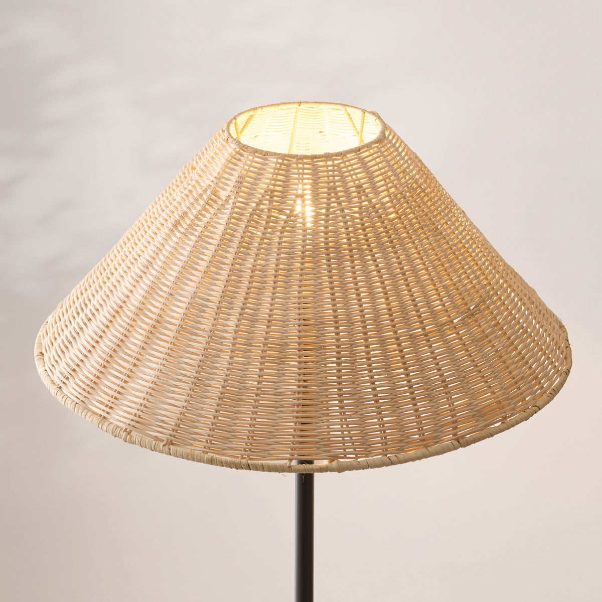 Close-up of the lit natural rattan woven shade on the matt black Arlo floor lamp