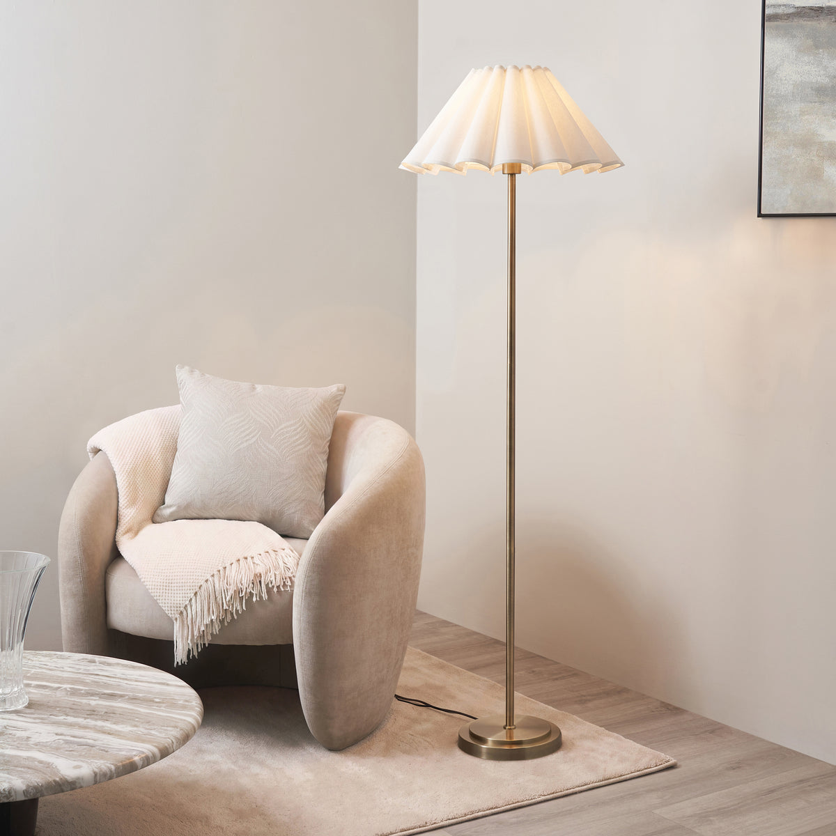 Brass Arlo & Ayla floor lamp lit beside a cream boucle armchair in a neutral living room