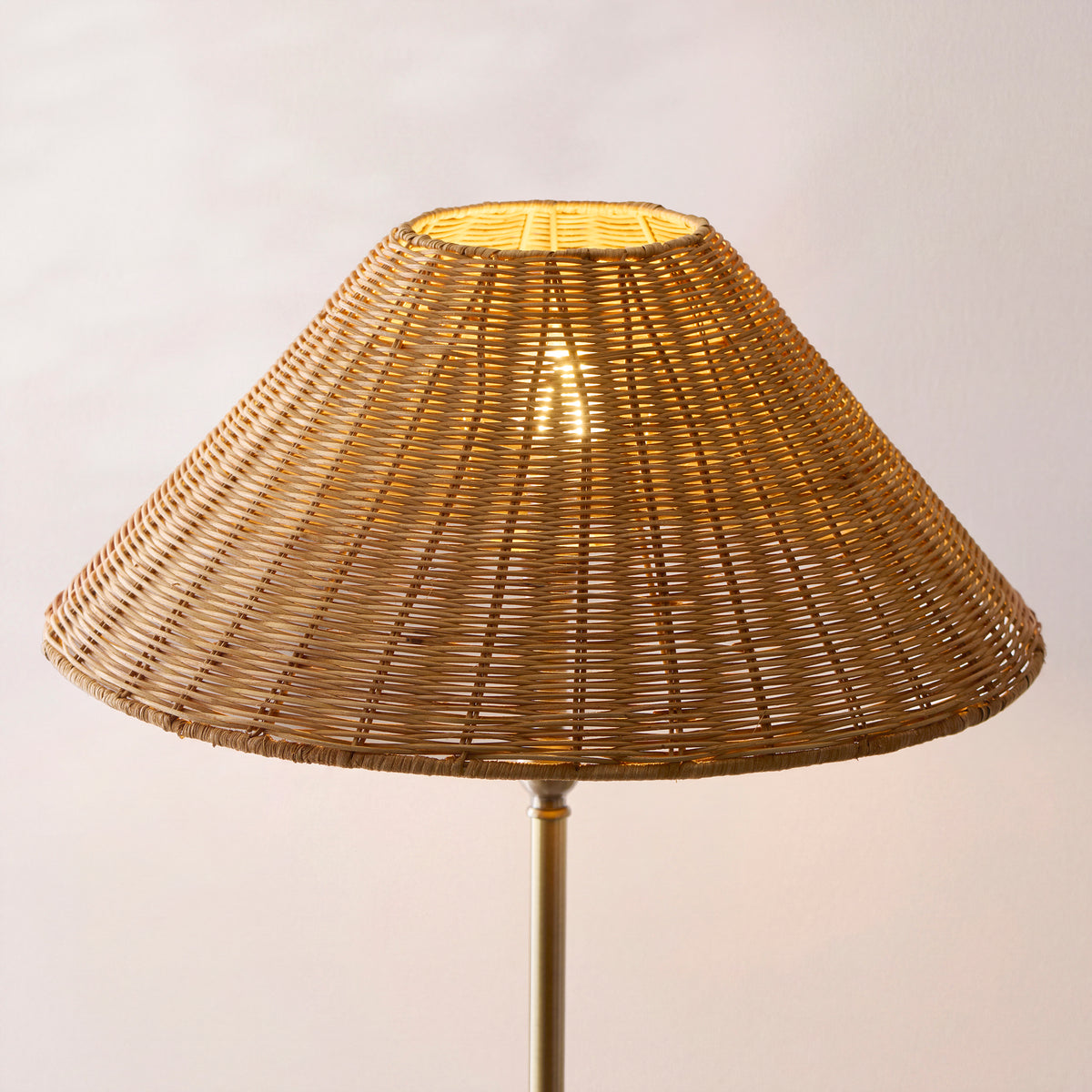 Close-up of the lit brown rattan woven shade above the antique brass Arlo stem
