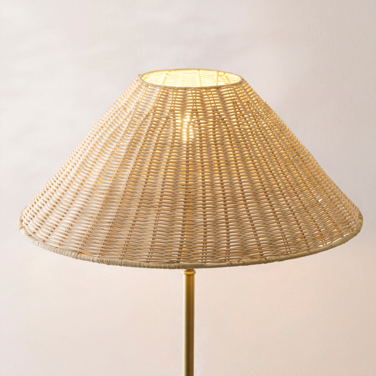 Close-up of the Arlo lamp's woven rattan coolie shade glowing warmly above its brass stem