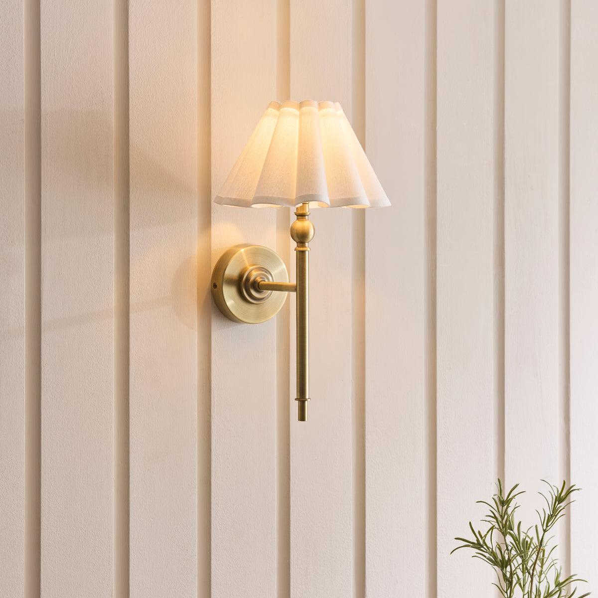 Sylvie brass wall light glowing softly against vertical panelling in a neutral interior