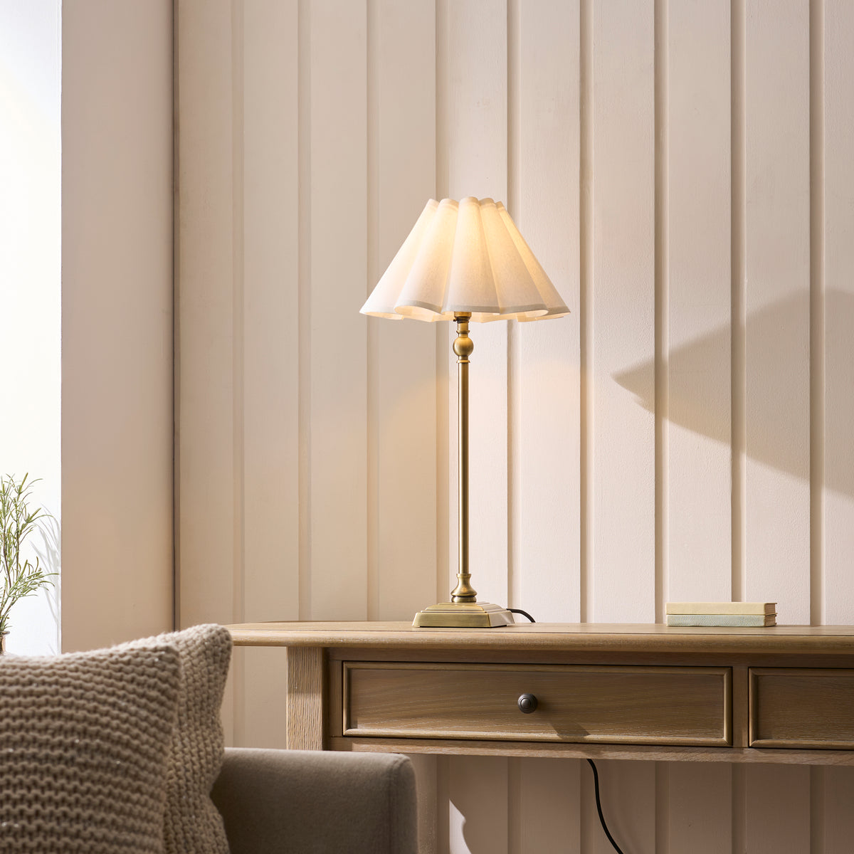 Sylvie brass table lamp lit on a wooden console table against cream panelling