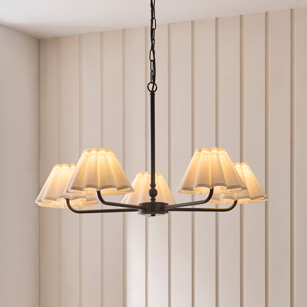 Sylvie five-light black pendant lit from below, its pleated shades casting warm light