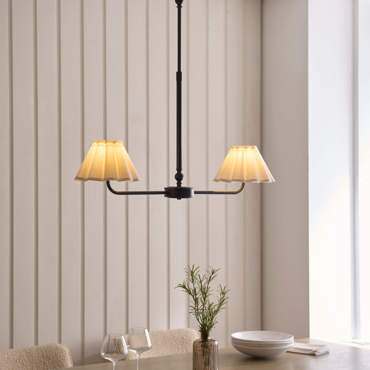 Sylvie black linear pendant lit above a dining table set with bowls, glasses and a rosemary sprig