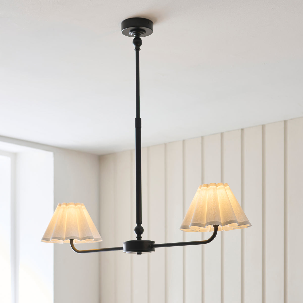 Sylvie black linear pendant on an extended stem lit beside a bright window