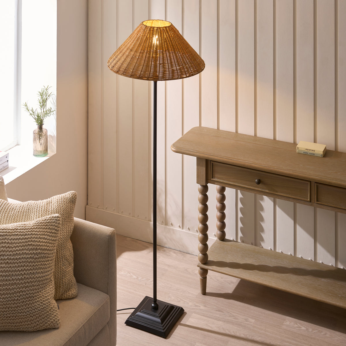 Jericho black rattan floor lamp glowing beside a window and wooden table