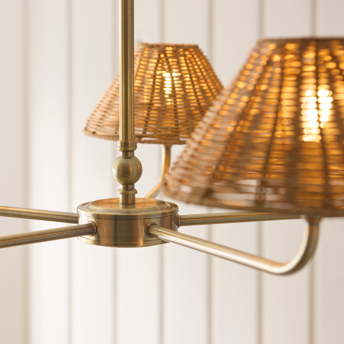 Antique brass hub and curved arms of the Jericho chandelier with glowing rattan shades