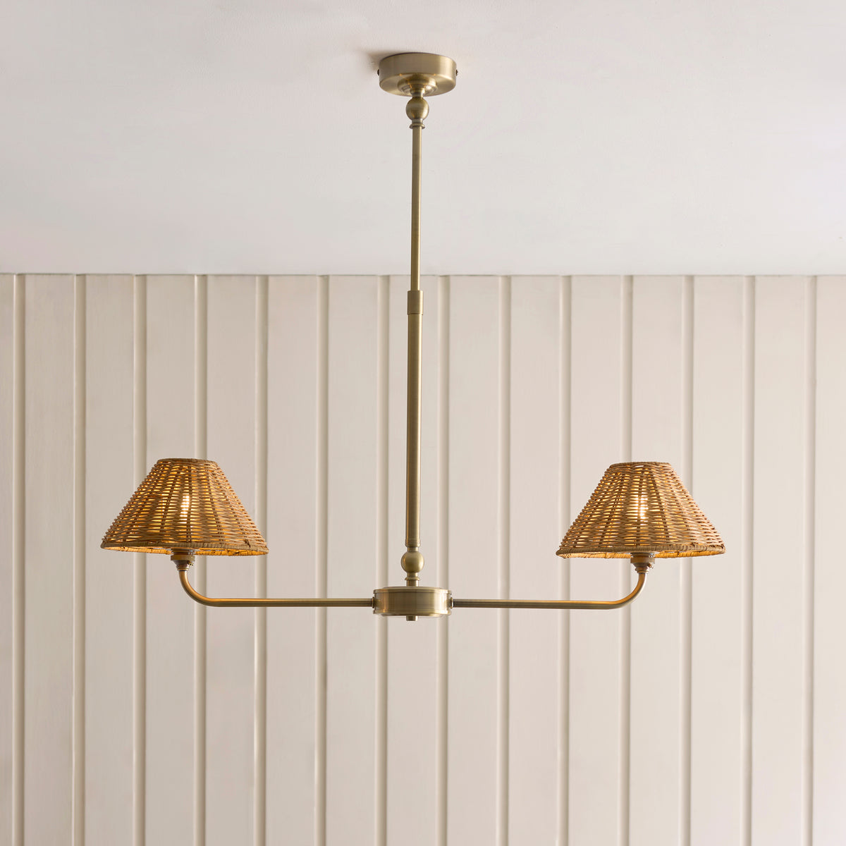 Jericho antique brass linear pendant hanging below a panelled ceiling with rattan shades lit