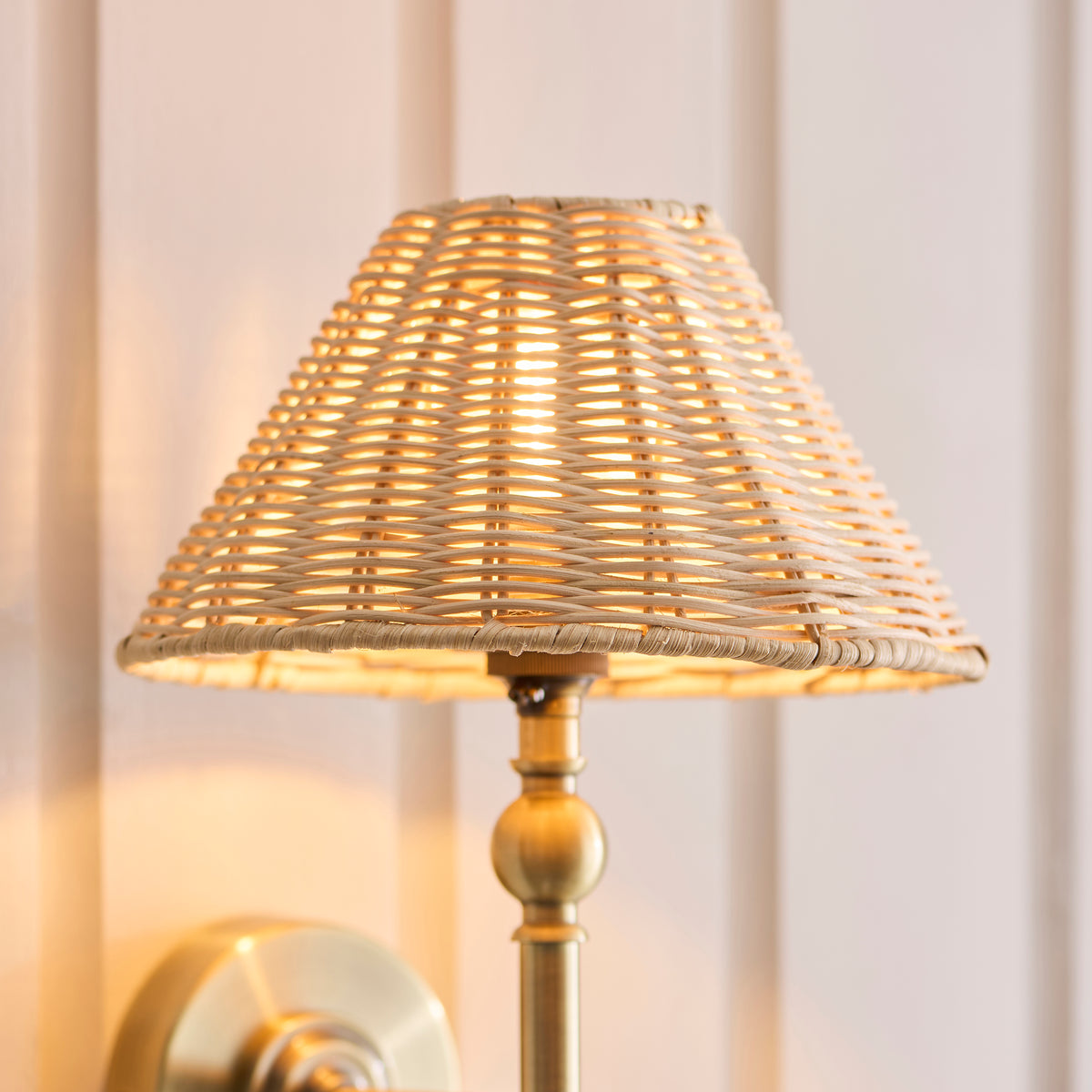Close-up of the lit natural rattan shade above the Jericho wall light's brass stem