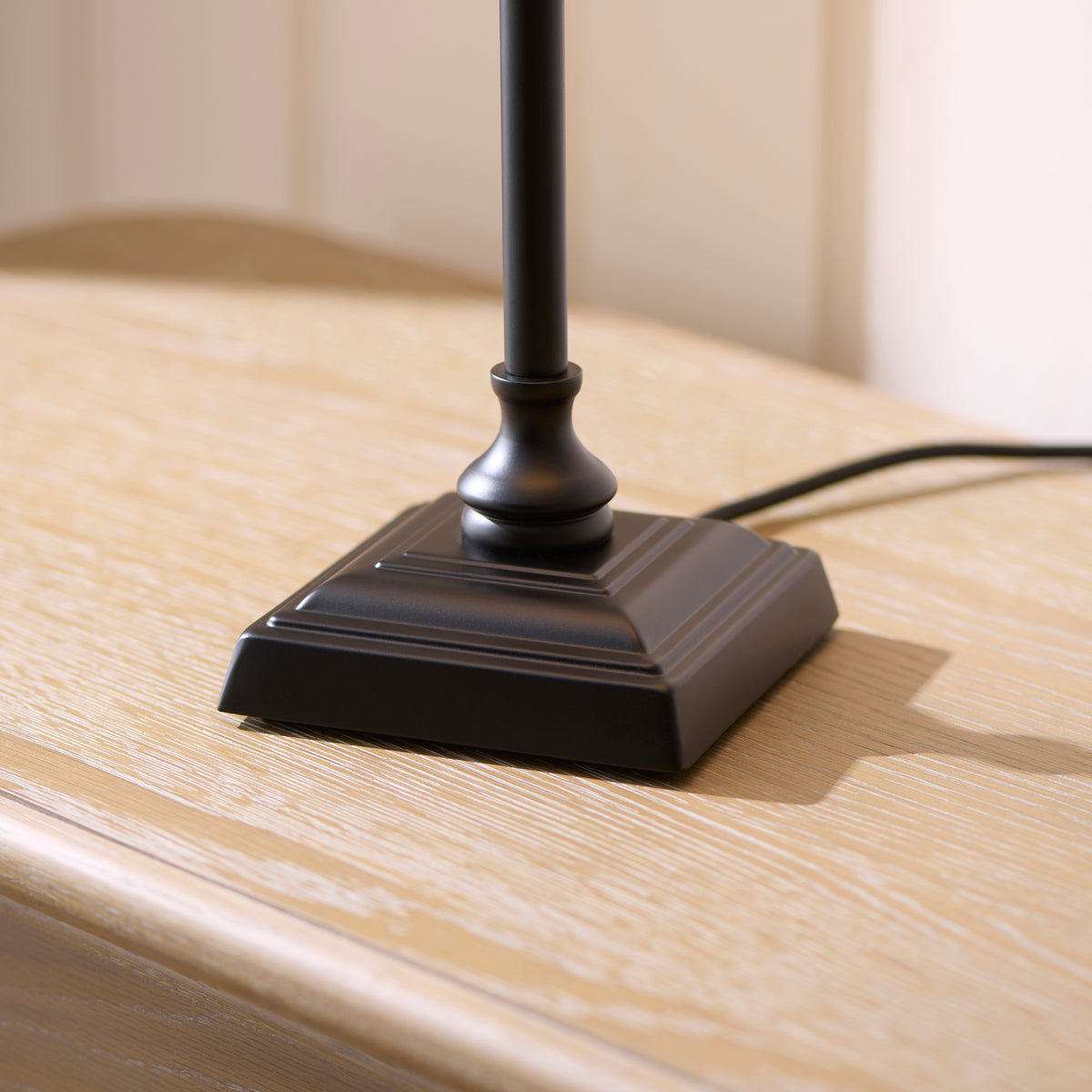 Stepped square black base of the Jericho table lamp on a pale wood surface