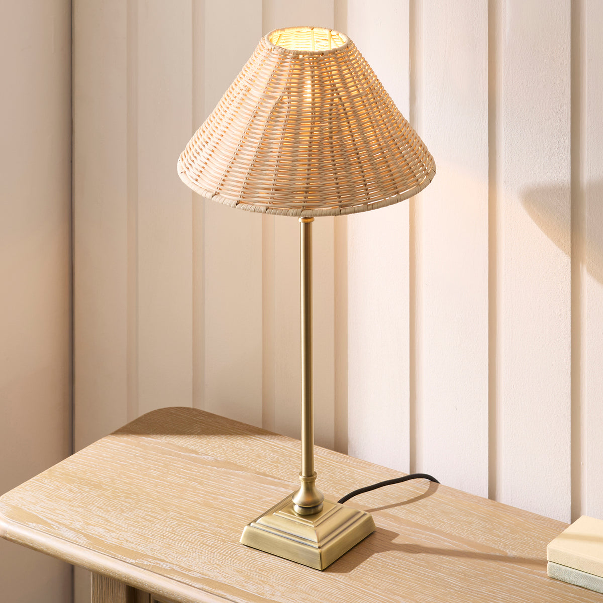 Jericho table lamp glowing on a limed oak table, brass stepped square base and rattan shade