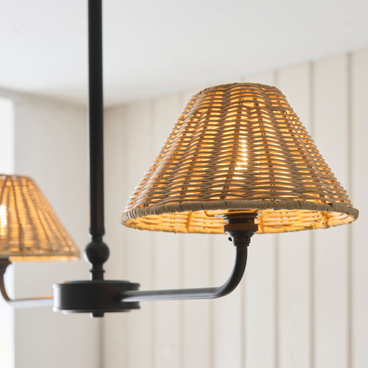 Close-up of a warmly lit rattan coolie shade on the Jericho black linear pendant