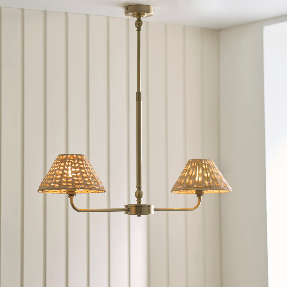 Jericho antique brass linear pendant glowing beneath a white ceiling beside a window