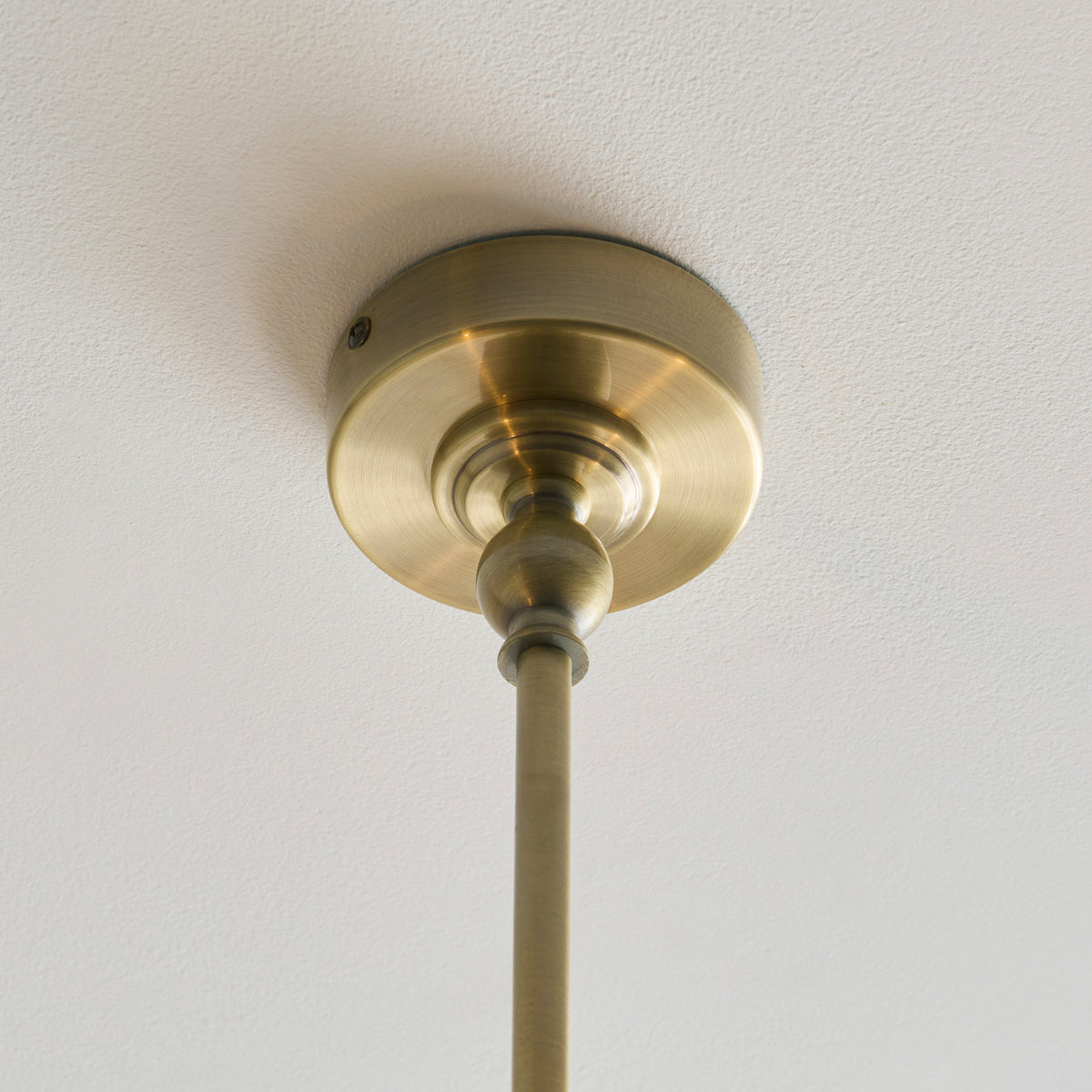 Antique brass ceiling rose and stem of the Jericho linear pendant on a white ceiling
