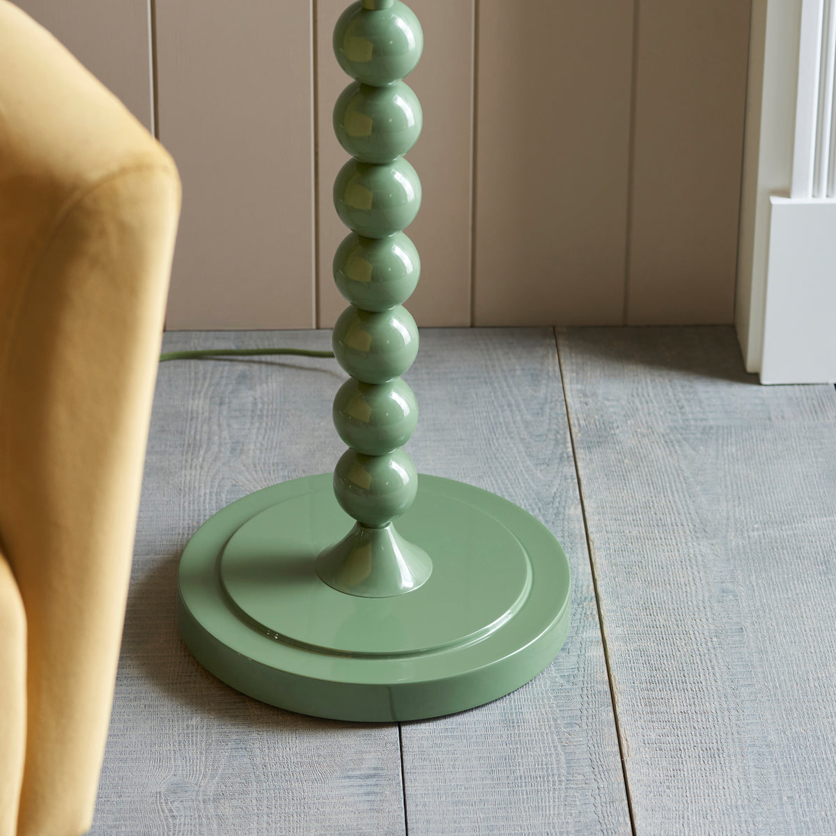 Round Cotswold green base of the Higgledy floor lamp on grey painted floorboards