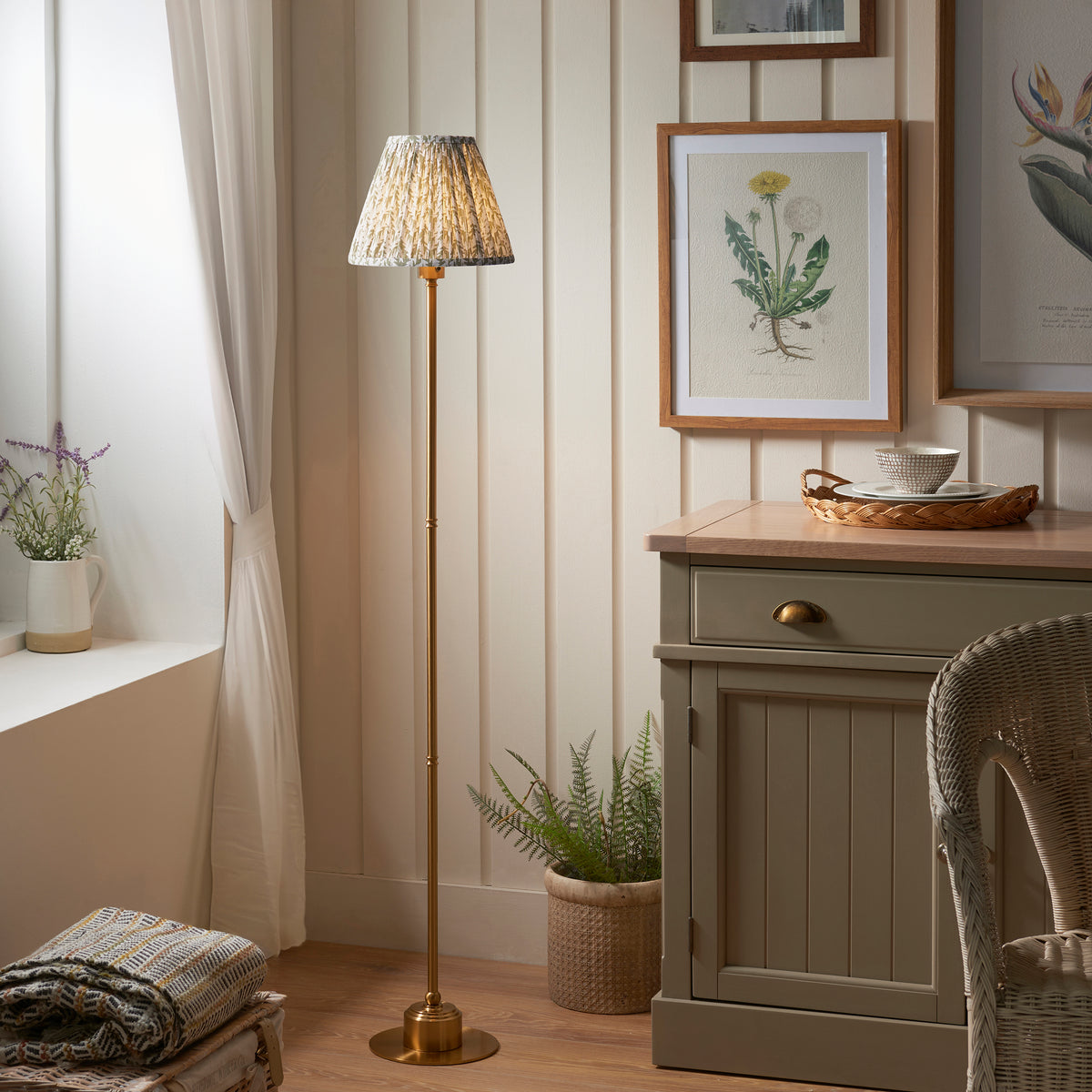 Burley brass floor lamp lit in a panelled hallway beside a sage cabinet and botanical print