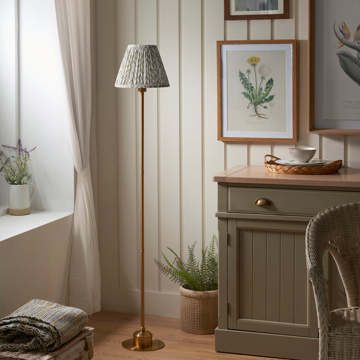 Burley brass rechargeable floor lamp unlit beside a green sideboard and wicker chair
