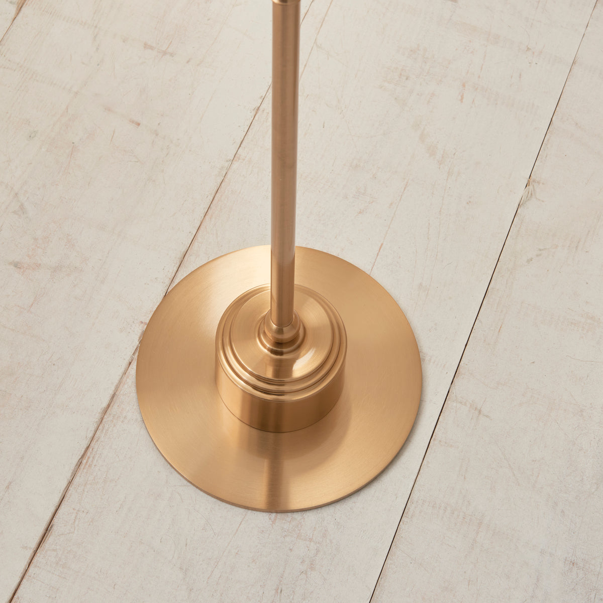 Round aged brass base of the Burley floor lamp on whitewashed floorboards
