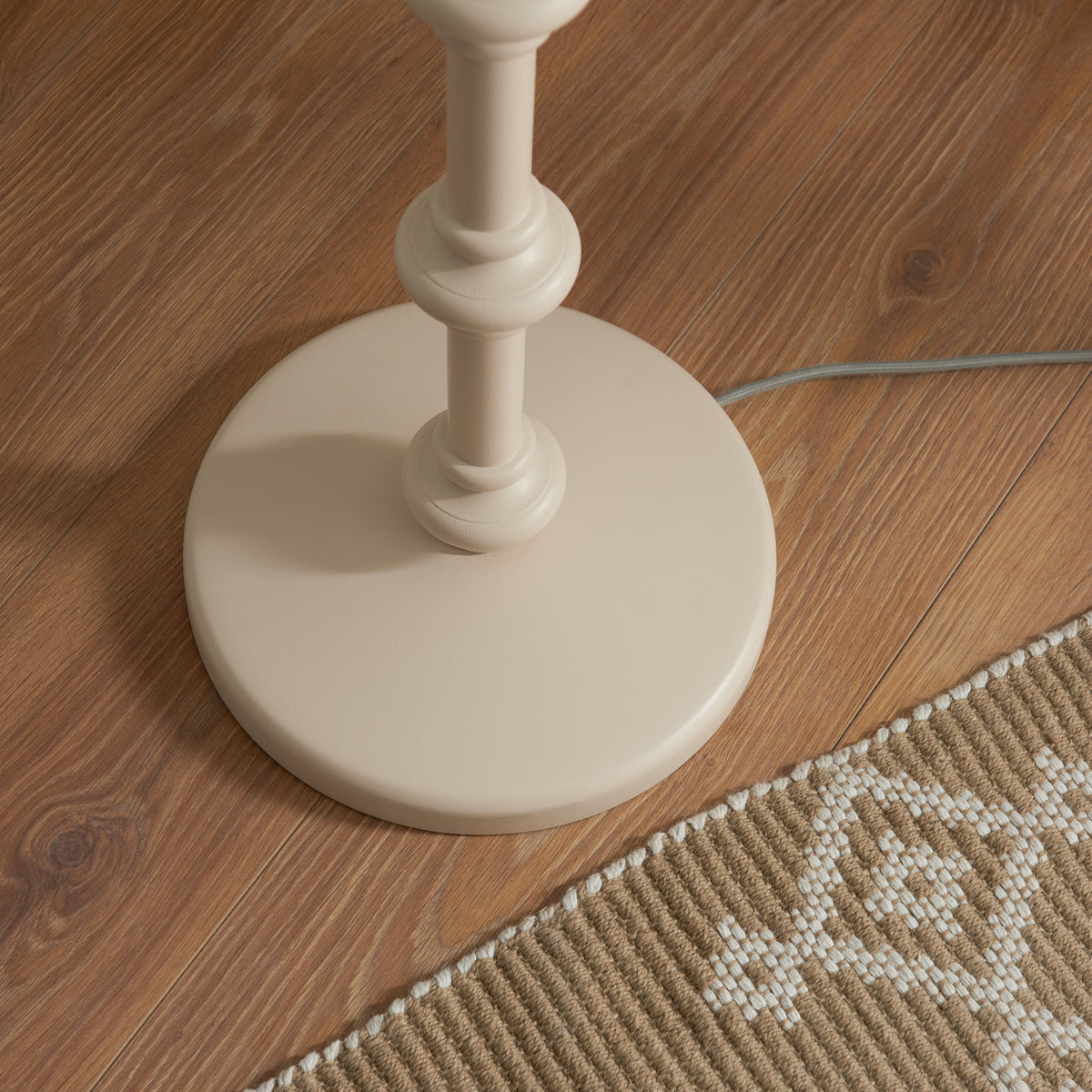 Round almond white base of the Carnaby floor lamp on wood flooring beside a woven rug