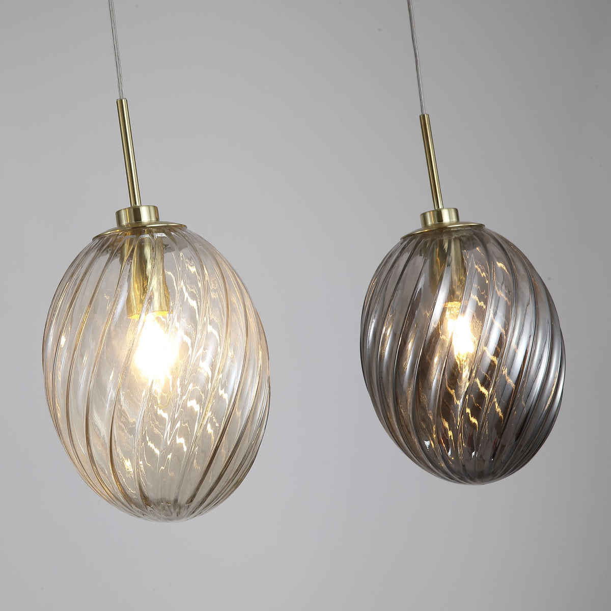 Close-up of two Whirl oval glass shades in amber and smoke with brass caps and glowing filament bulbs
