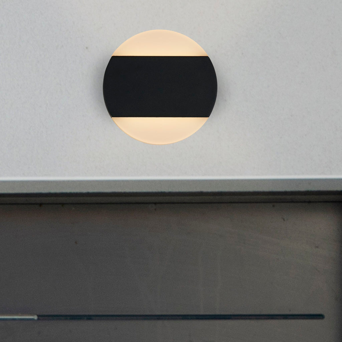Cavern black disc wall light glowing on a pale grey wall above a dark ledge