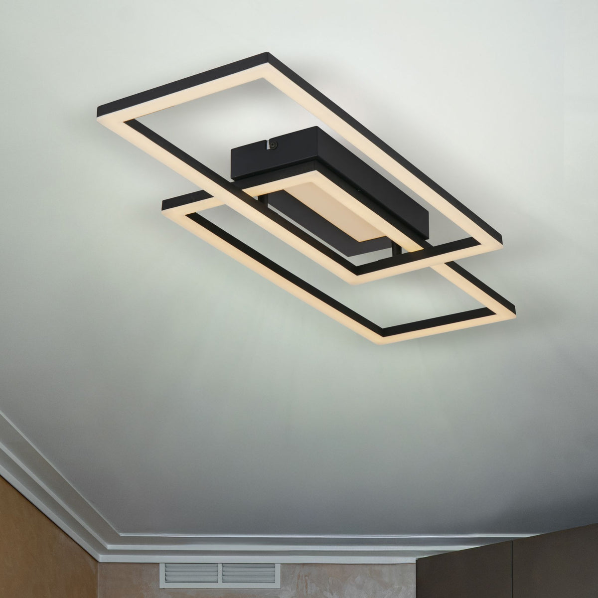 Ovaloid black frame LED ceiling light lit on a plain white ceiling above pale walls and coving