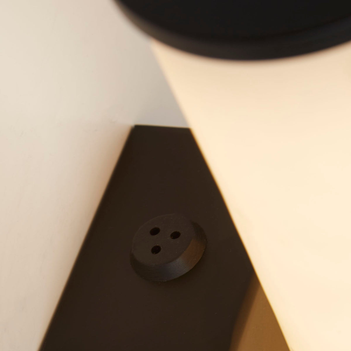 Detail of the Wales wall light's matt black bracket and button switch against the marble resin shade