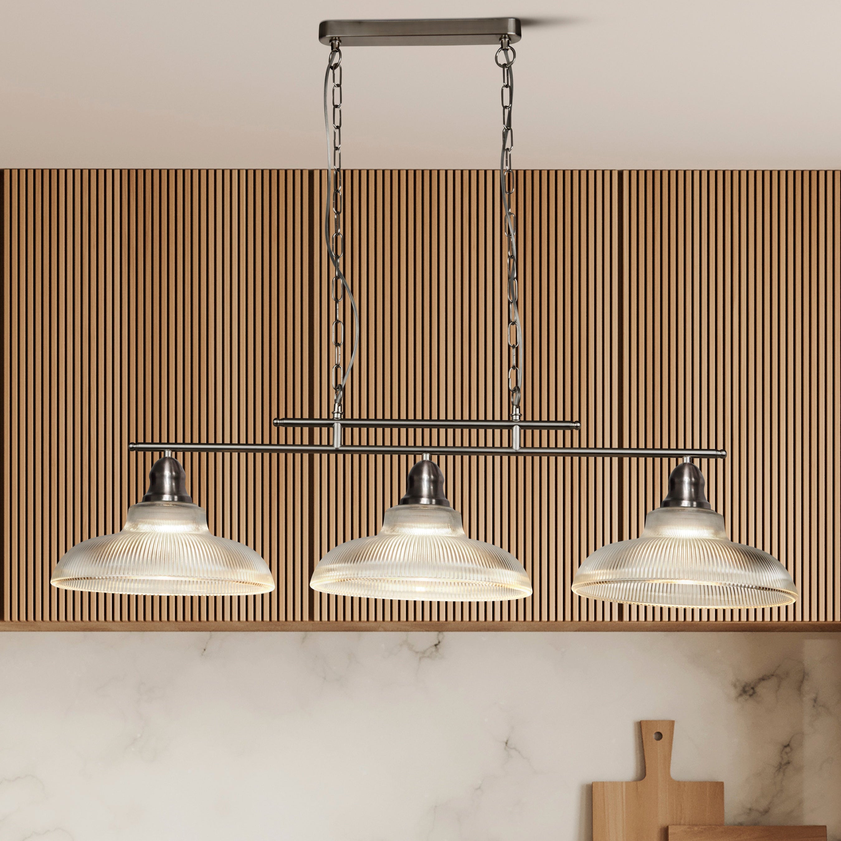 Modern kitchen pendant light fixture with three glass shades above a marble countertop.