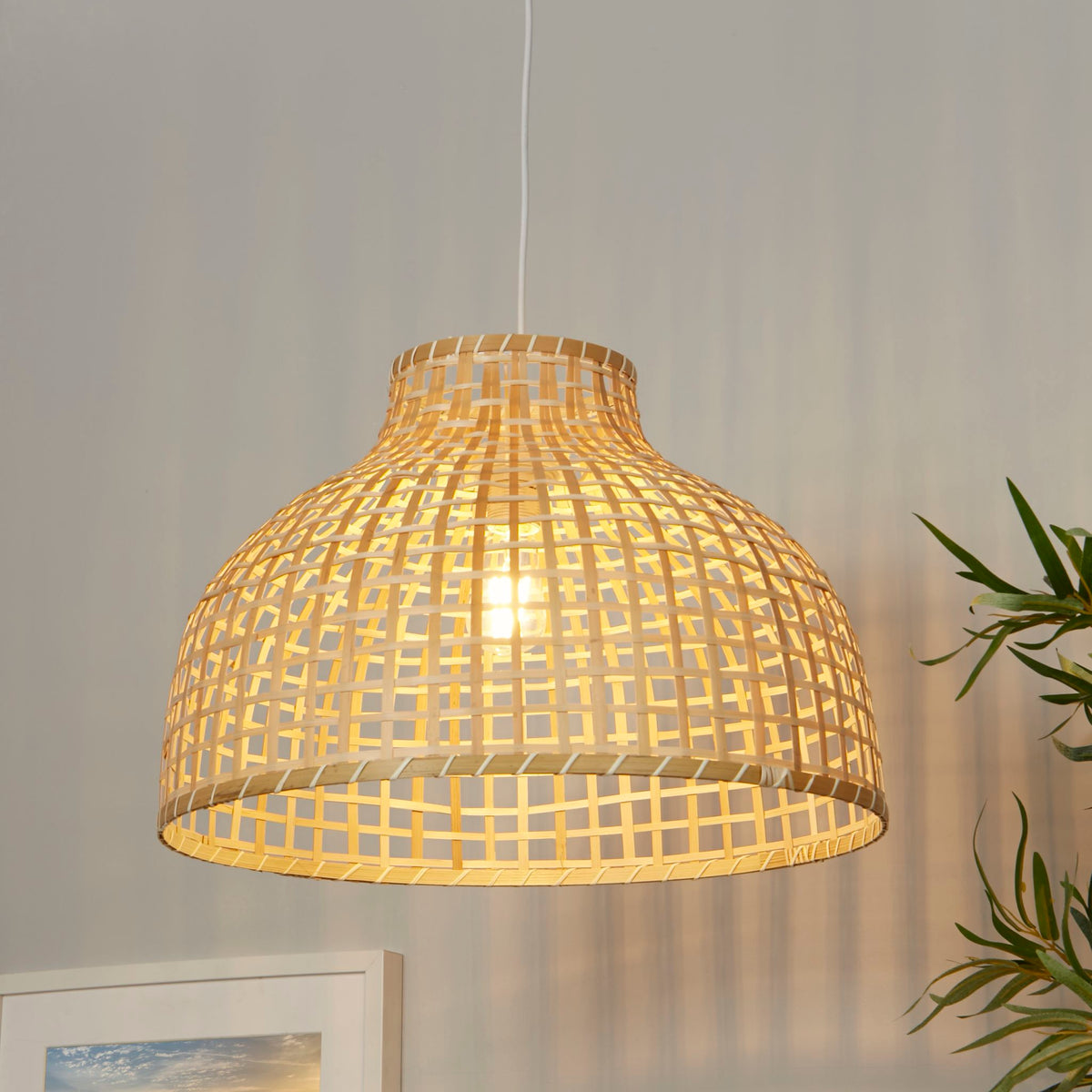 Bali bamboo pendant beside a framed print and green foliage on a soft grey wall