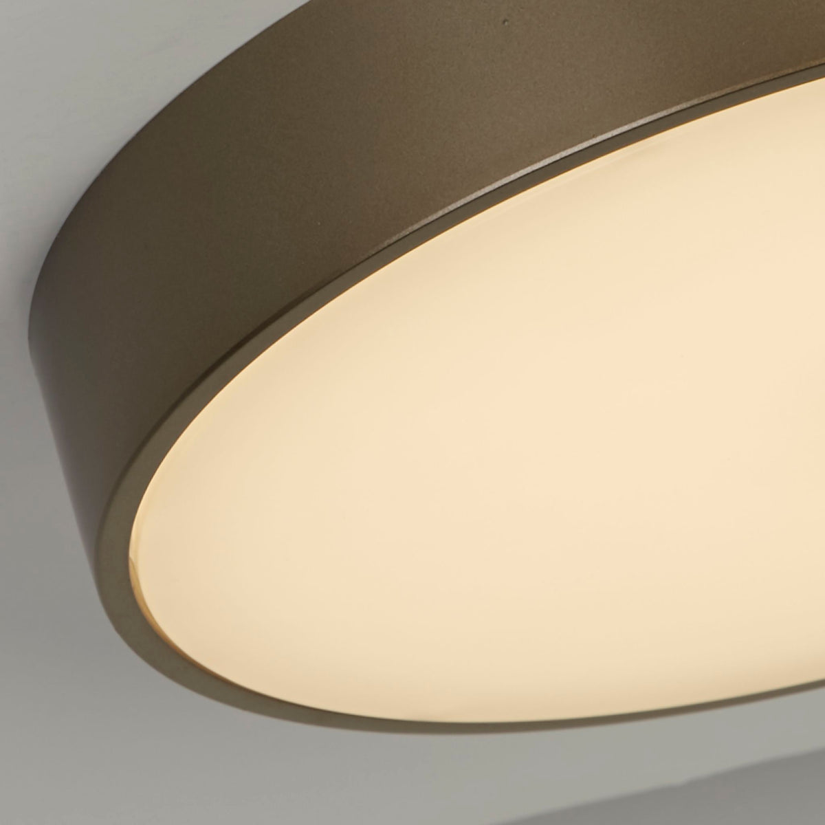 Detail of the Palma light's bronze drum rim curving over its softly glowing opal diffuser