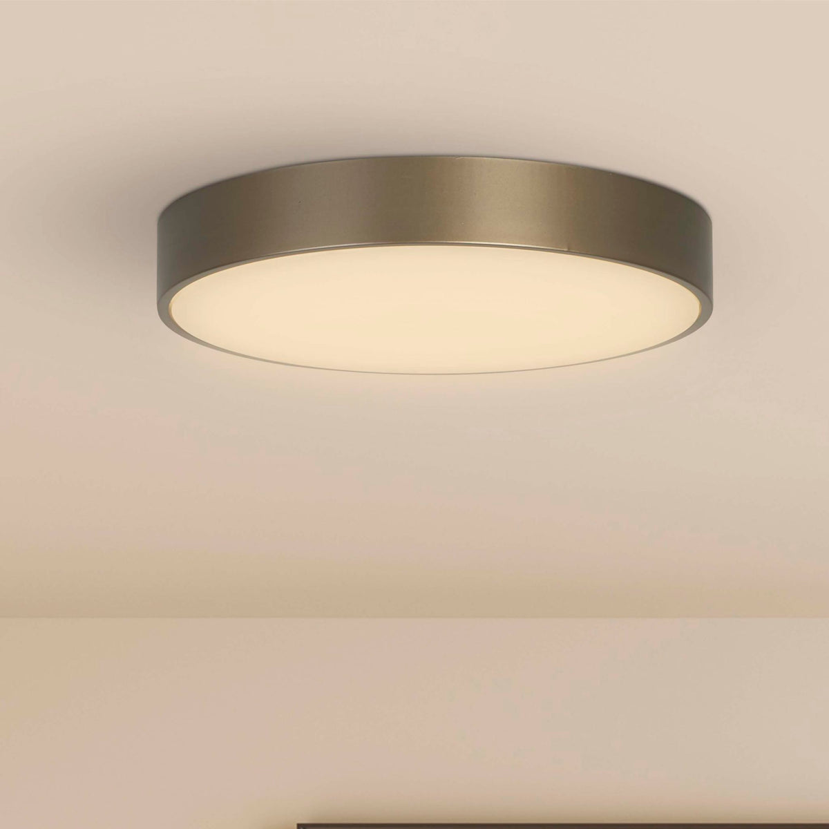 Palma bronze flush ceiling light lit on a plain ceiling in a warm minimalist neutral room