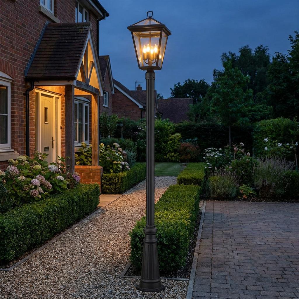Traditional Alford Place 4-light lamp post illuminates a gravel garden path and hedge at dusk.