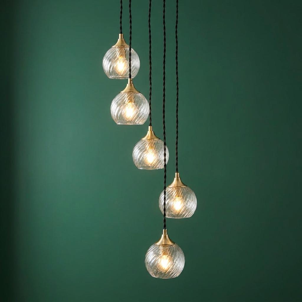 Five-light brass cascade pendant with ribbed glass globes suspended at varying heights against a dark green wall.