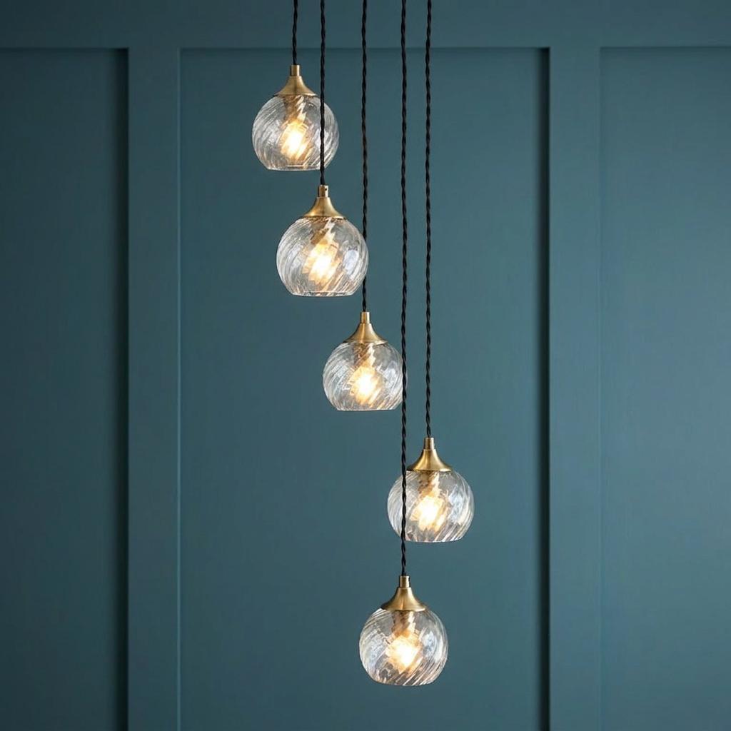 Cascading five-light brass pendant with ribbed glass globes against a dark teal paneled wall.