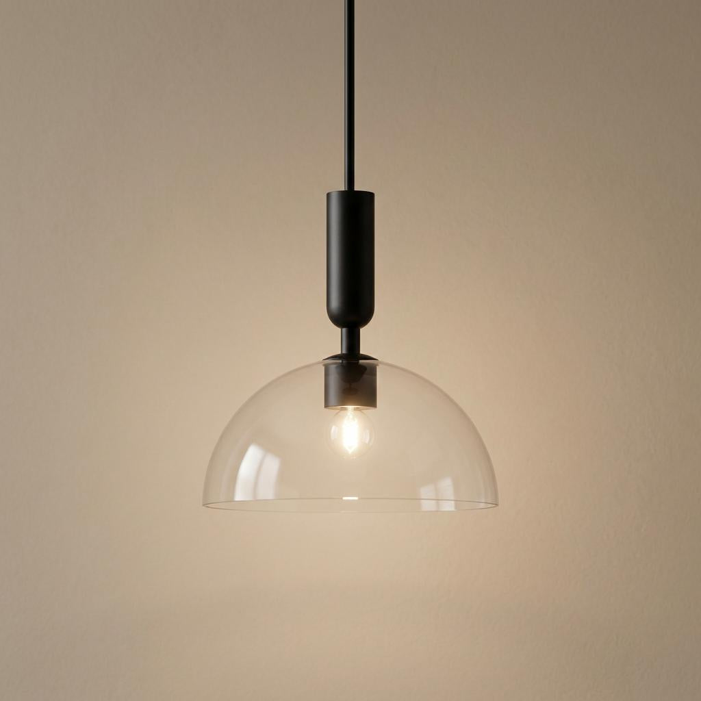 Alora Mood Jude Black Pendant Light with a clear glass dome shade and lit bulb against a neutral wall.