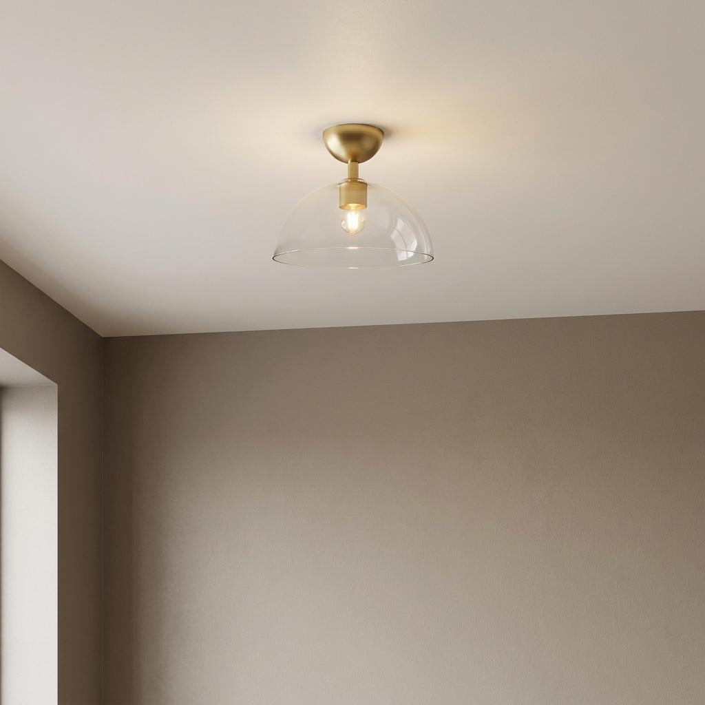 Modern gold semi-flush ceiling light with a clear glass dome shade against a neutral wall.