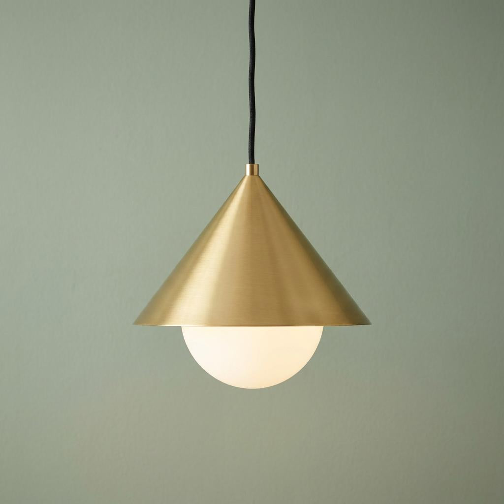 Modern gold conical pendant light with an opal glass globe shade hanging against a muted green wall.