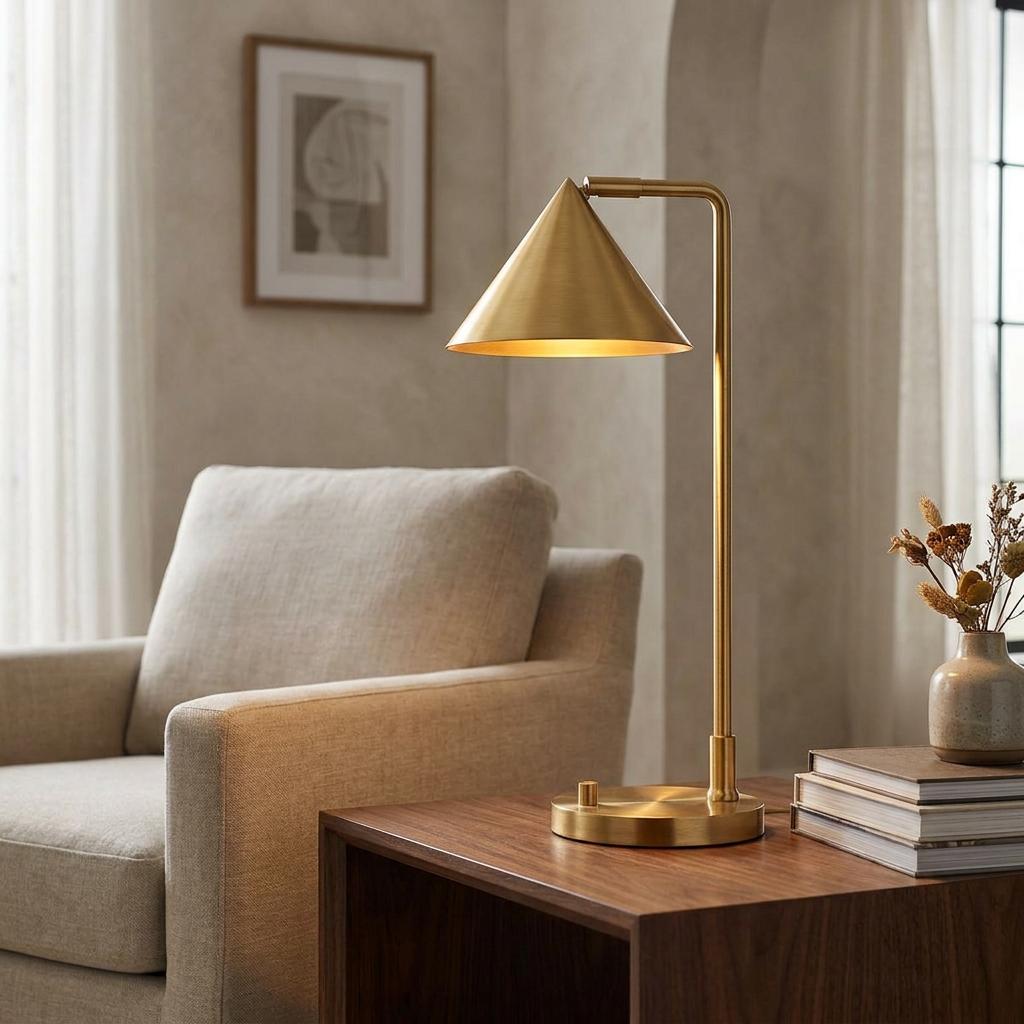 Alora Mood Remyck gold table lamp with a conical shade on a wooden side table next to a beige armchair.