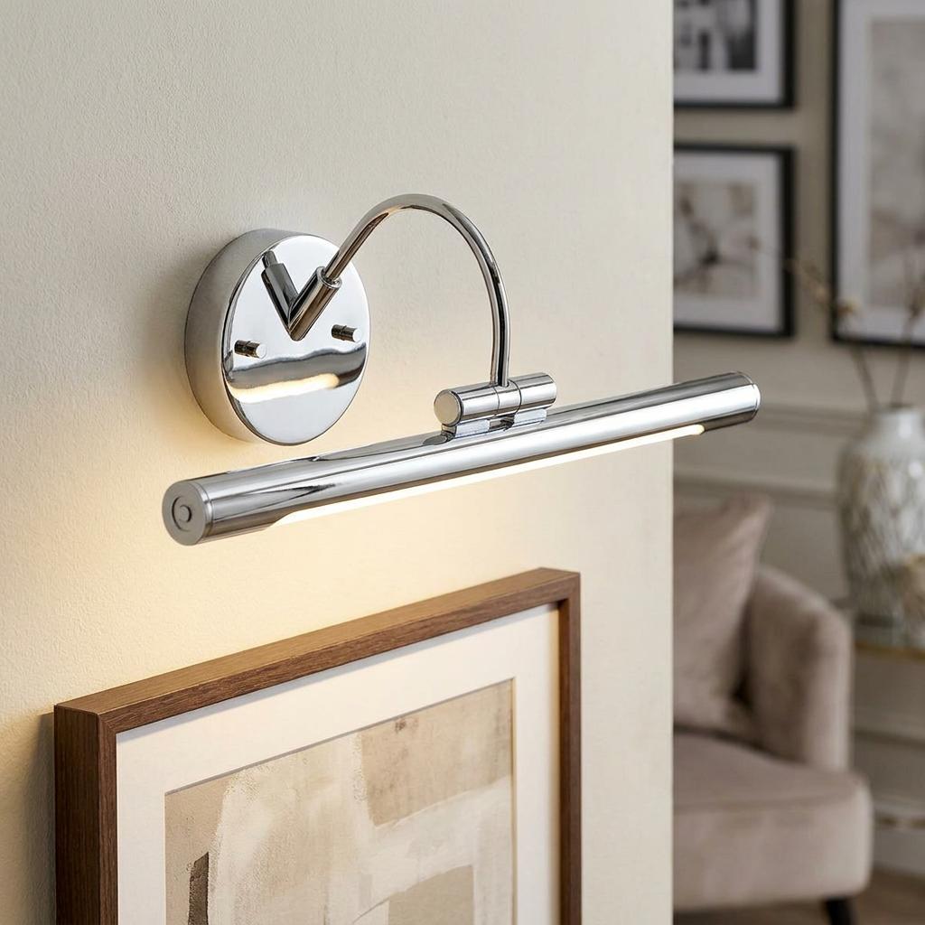 Polished chrome LED picture light with a curved arm, mounted on a wall above a framed piece of art.