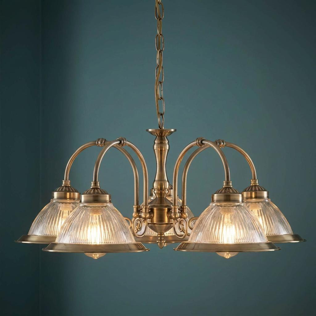 Five-light antique brass pendant chandelier with ribbed glass shades against a dark teal wall.