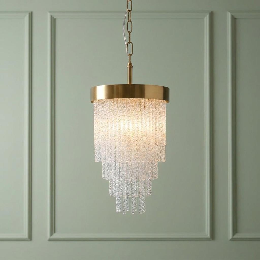 Tiered brass and glass rod pendant light glowing against a sage green paneled wall.